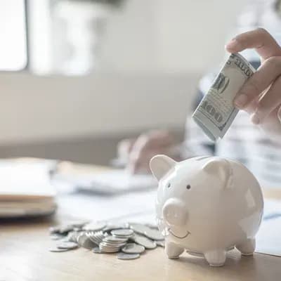 Épargne pour achat immobilier : main insérant un billet dans une tirelire avec des pièces sur une table