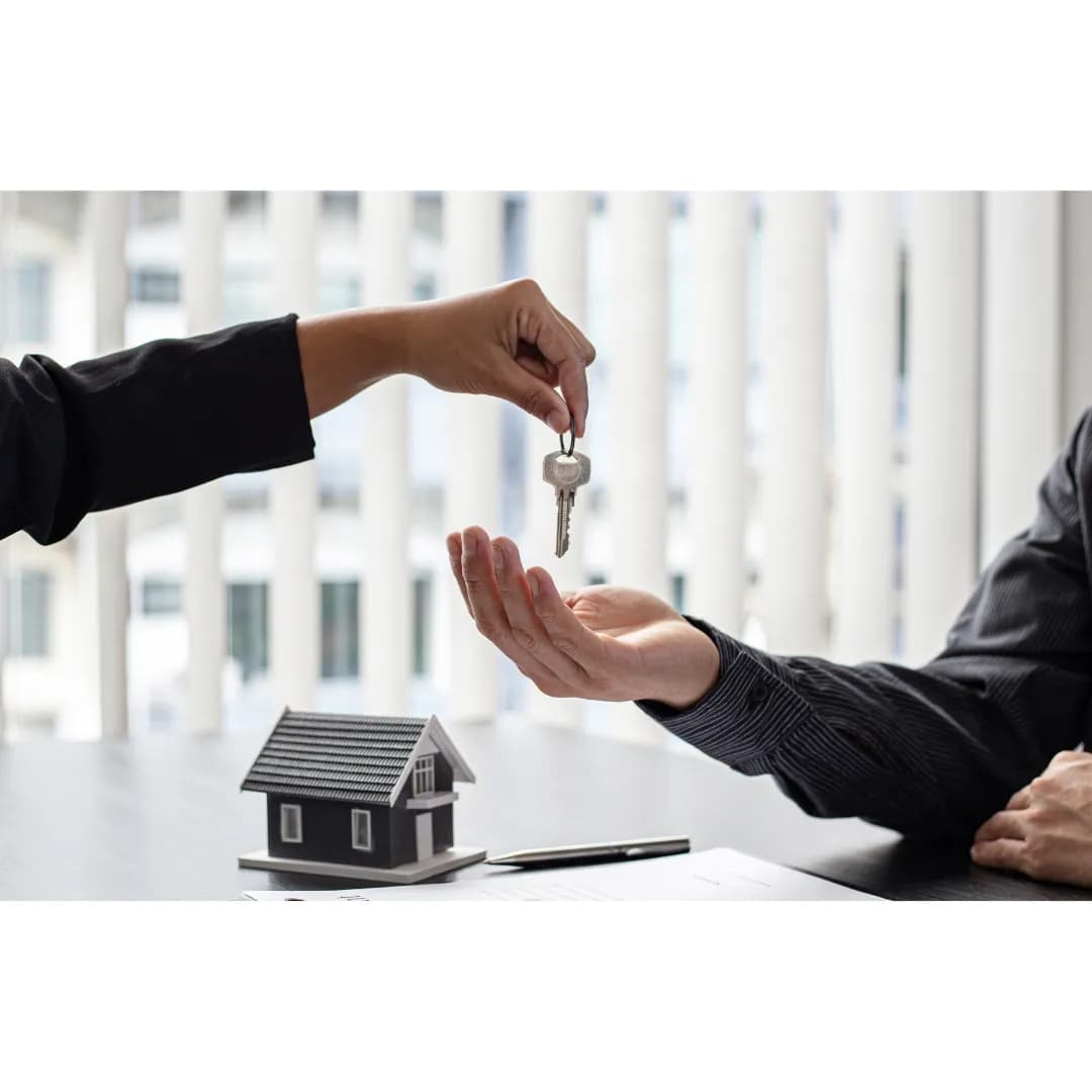 Remise de clés entre deux personnes lors d'un achat immobilier via une SCI, avec une maison miniature et un contrat signé sur la table.