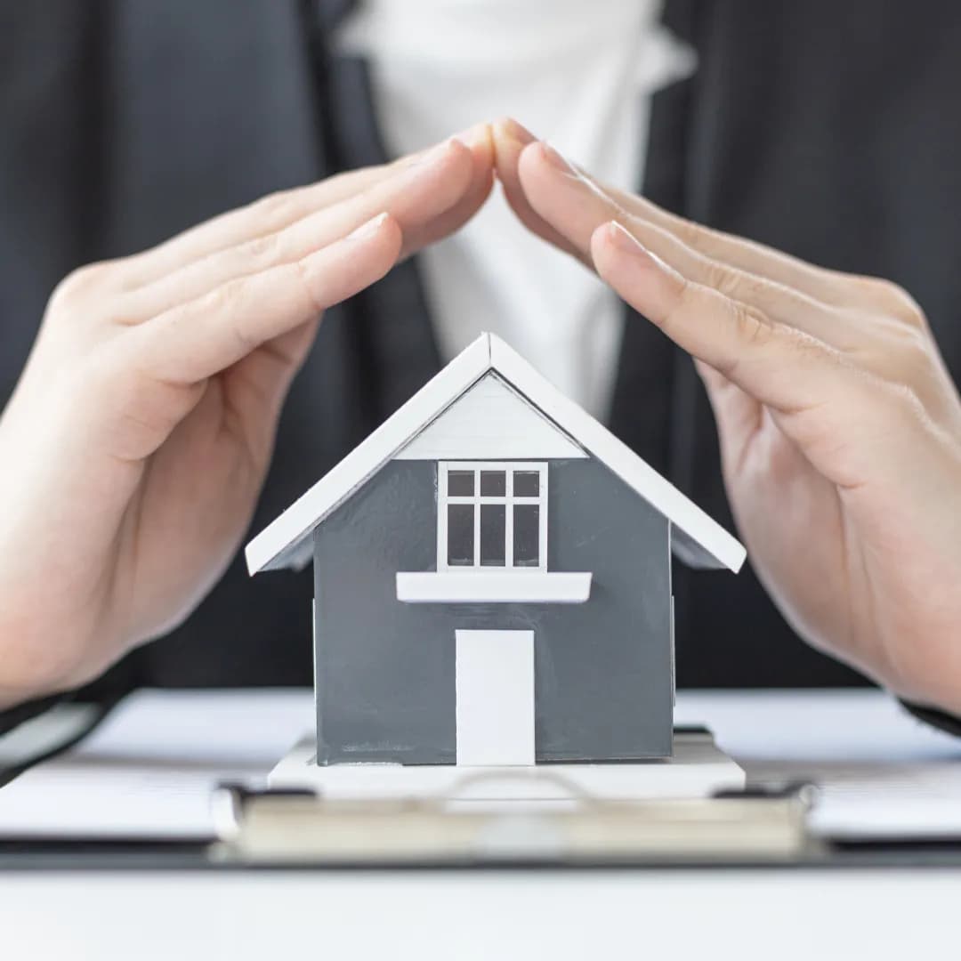 Assurance emprunteur : mains protégeant une maison miniature, symbolisant la sécurité d'un prêt immobilier et la protection financière