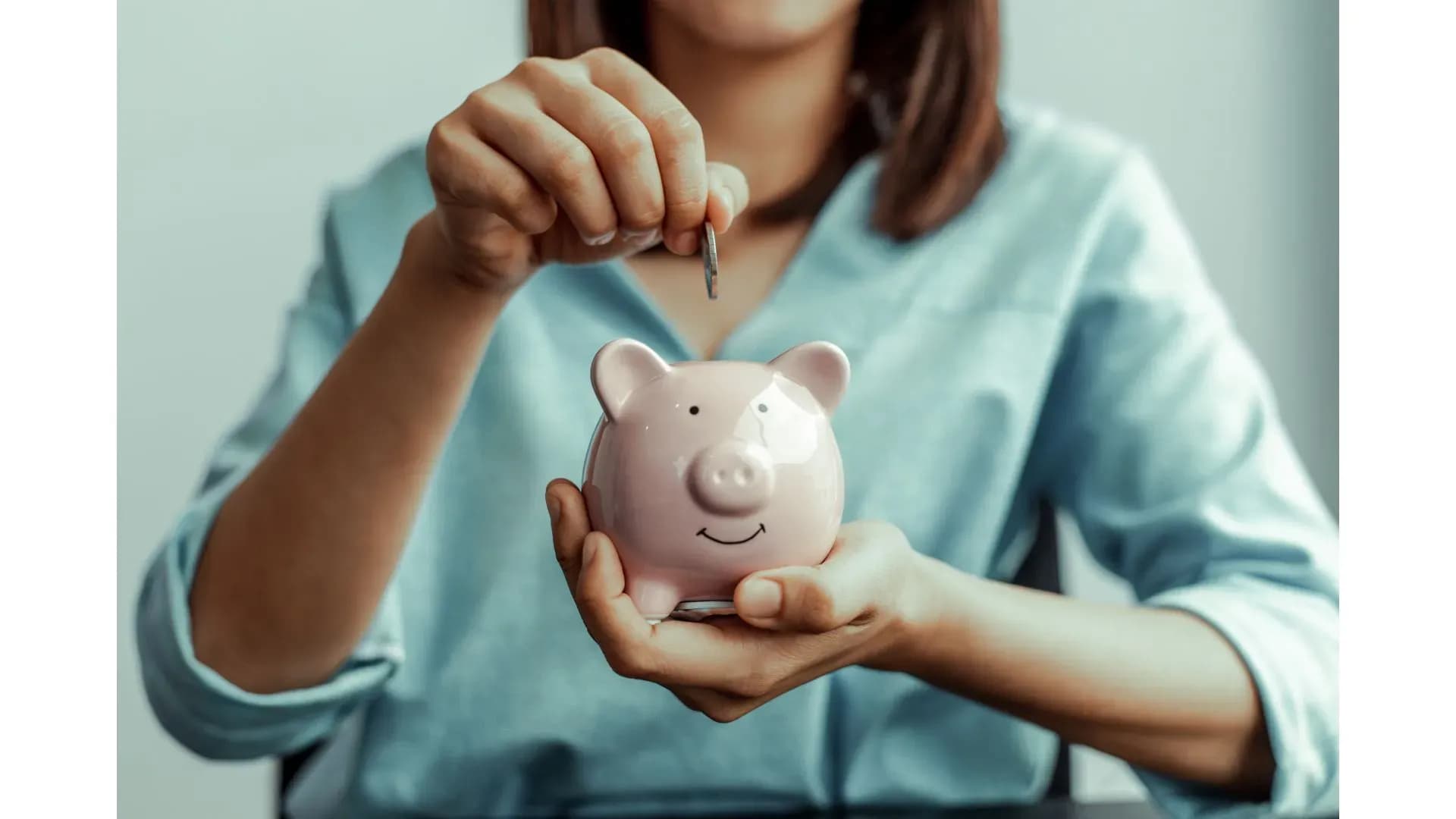 Femme plaçant une pièce dans une tirelire pour épargner en vue d’un achat immobilier